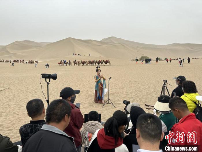 圖為2023年4月底，敦煌大漠“逐舞者”奧楠在鳴沙山月牙泉景區(qū)視頻直播，吸引游人圍觀。　馮志軍 攝